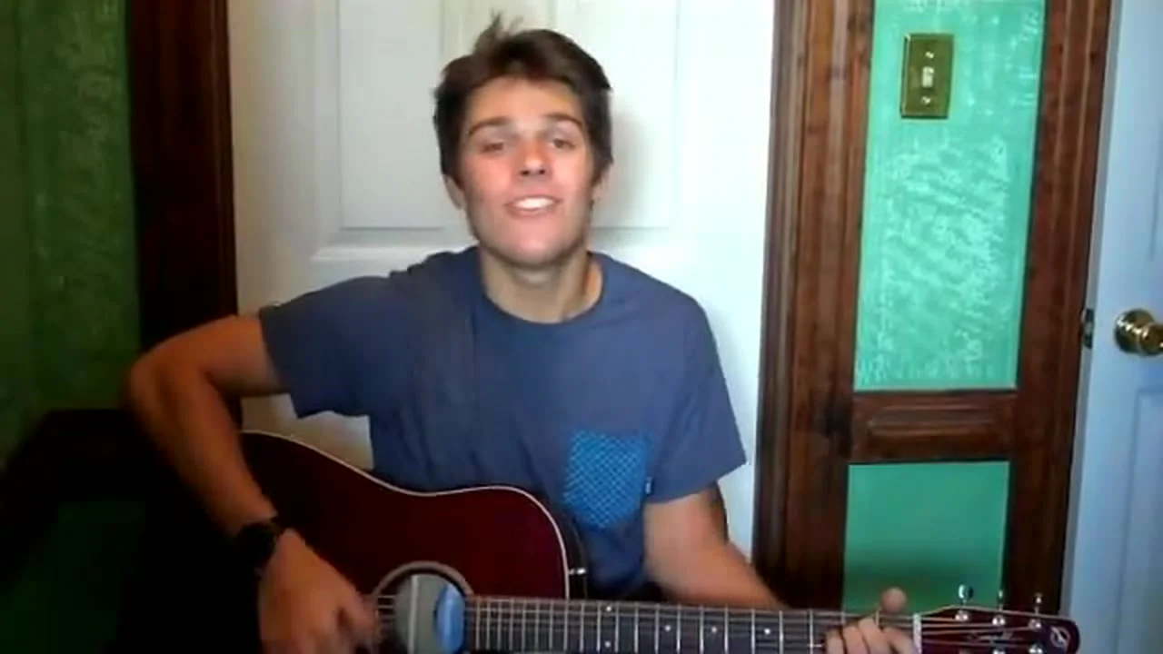 Cole in a blue t-shirt singing Beautiful with his acoustic guitar