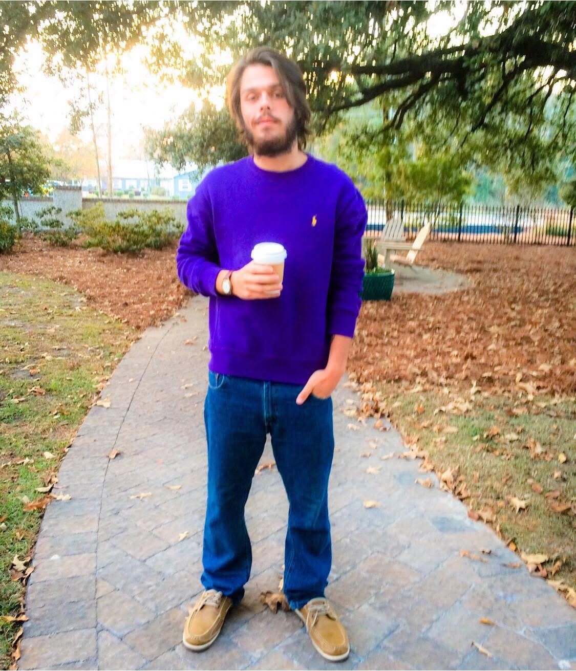 Julius Cole Rassin in a purple sweater holding a coffee cup on a park path in fall