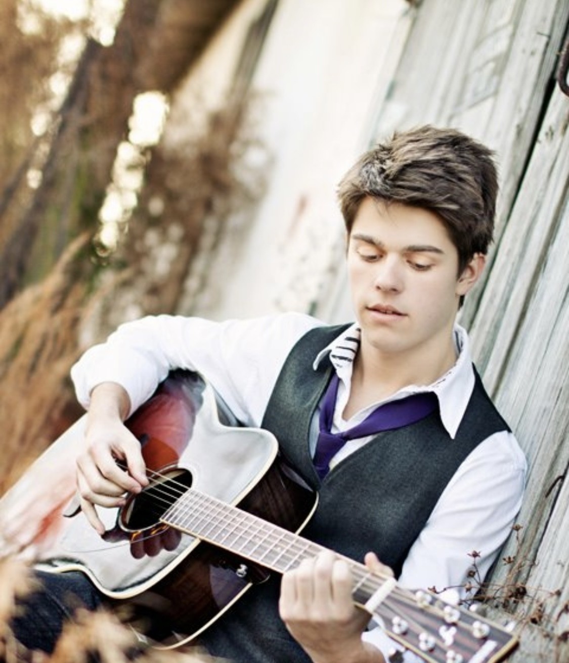 Julius Cole Rassin as a teen, acoustic guitar, against a weathered barn wall