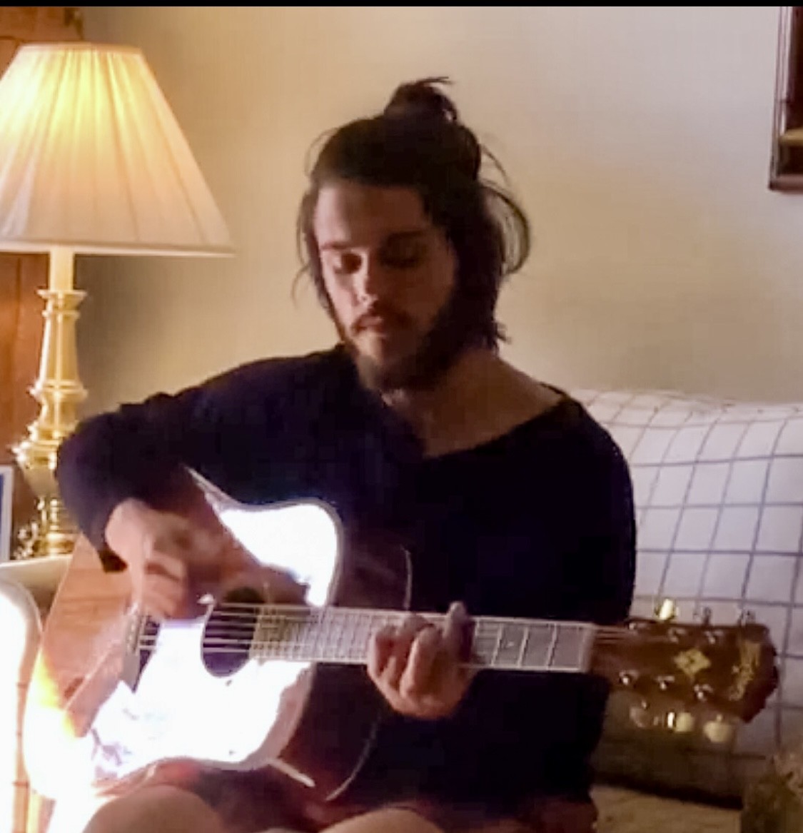Julius Cole Rassin playing acoustic guitar in a lamp-lit living room