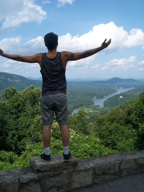 Julius Cole Rassin at a mountain overlook, arms outstretched, looking out over a river valley