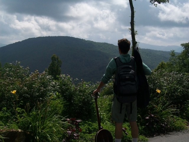 Julius Cole Rassin with a backpack and acoustic guitar at a Blue Ridge mountain overlook