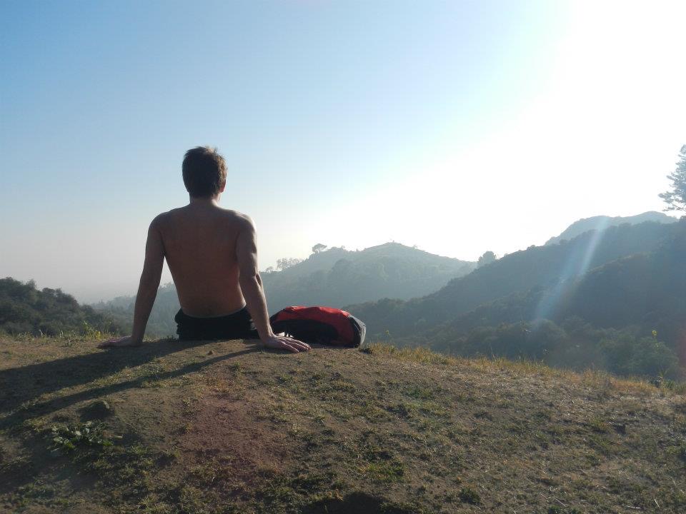 Julius Cole Rassin sitting on a hilltop at sunrise, looking out toward distant mountains