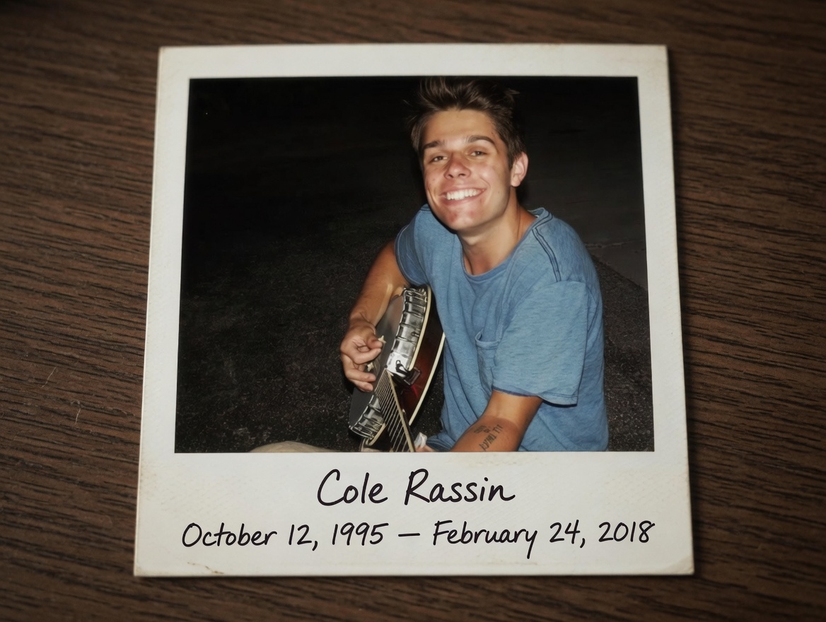 Cole Rassin, smiling with his banjo: polaroid with his name and dates handwritten below the photo, resting on a dark wood desk.